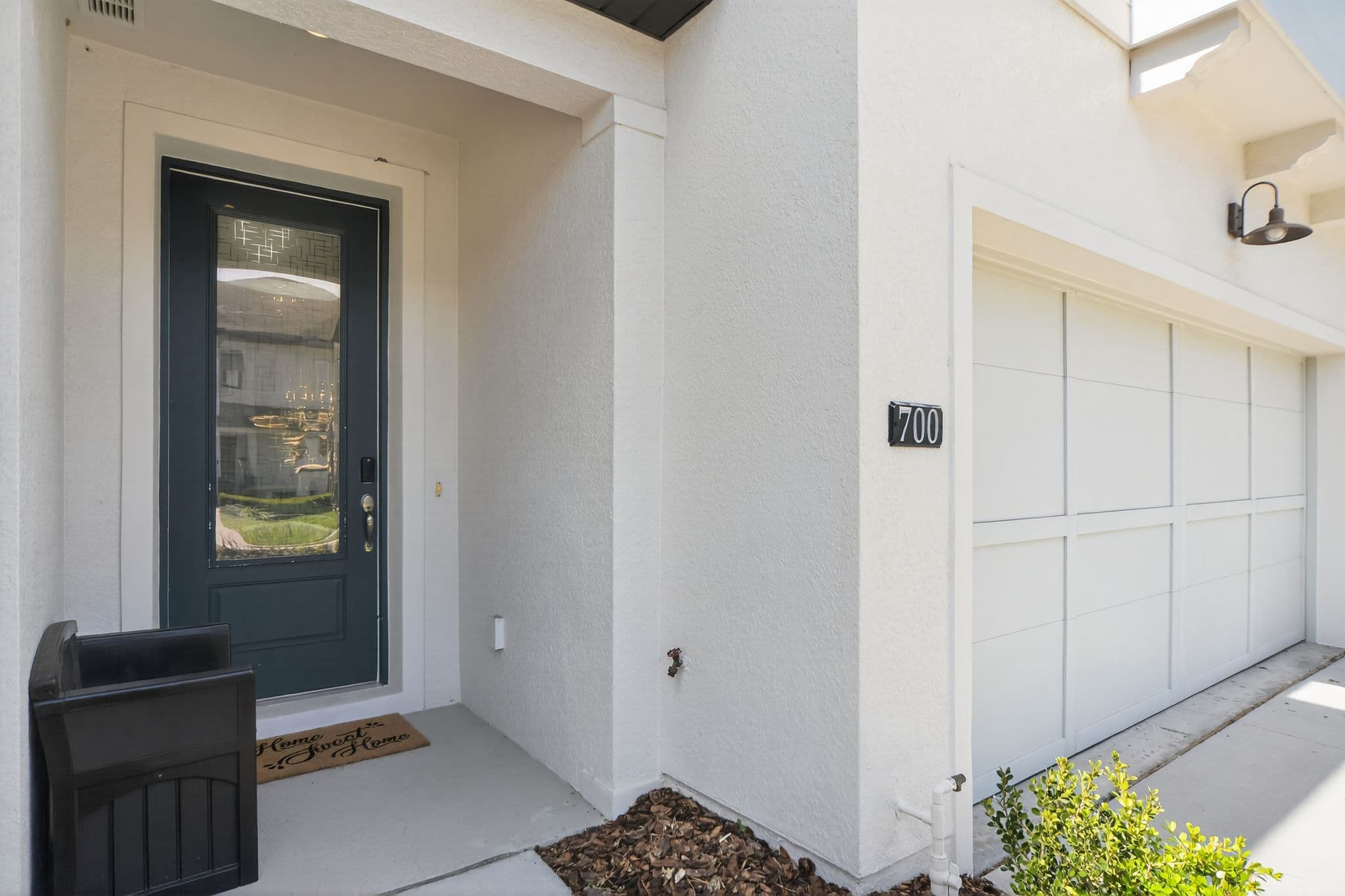 White stucco home entrance with a dark blue door, address 700, and white garage door.