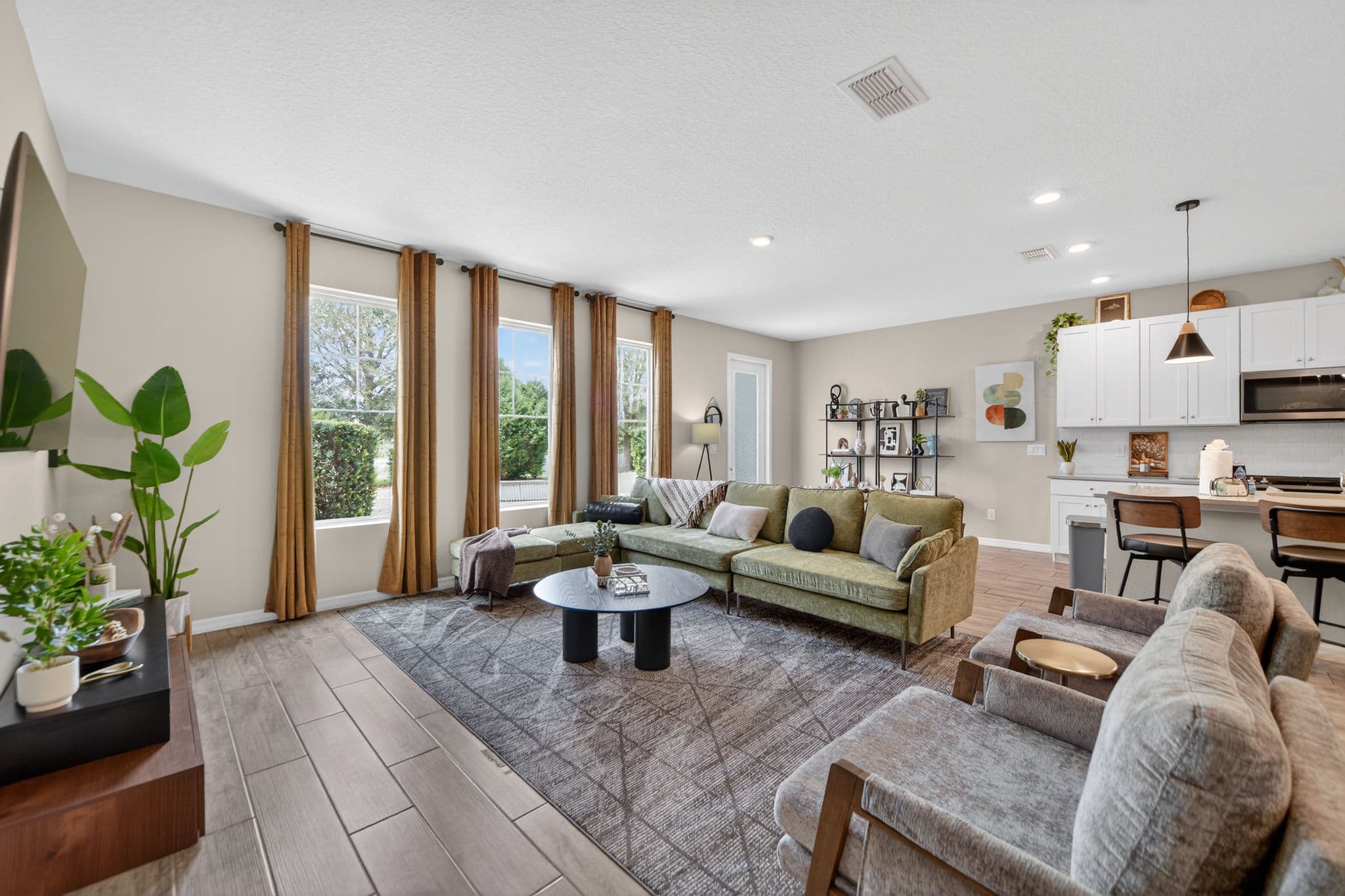 Bright living room with a green sectional, grey armchairs, and large windows with gold curtains.