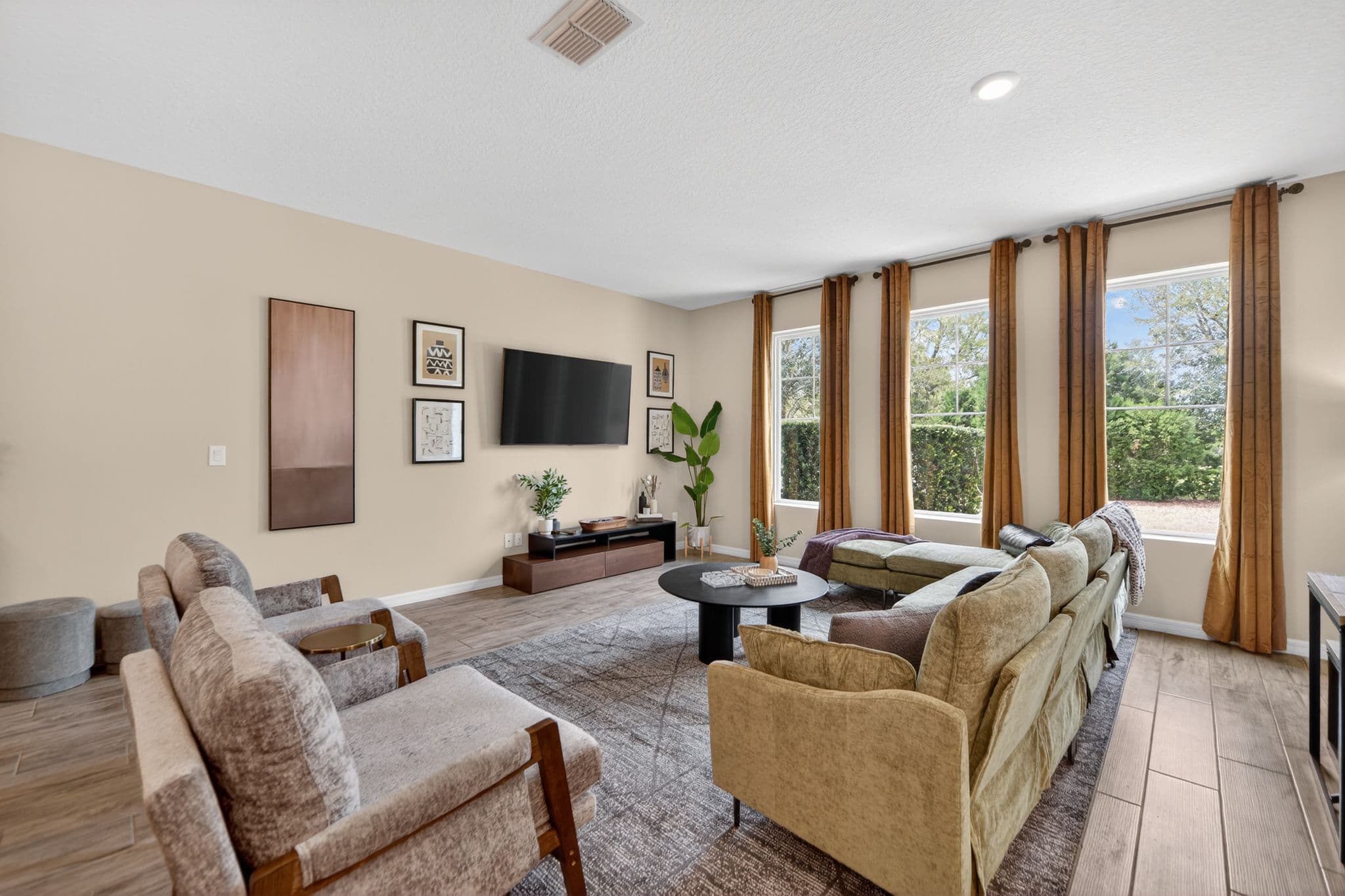 Modern living room with tan sectional, grey armchairs, black coffee table, and large windows.