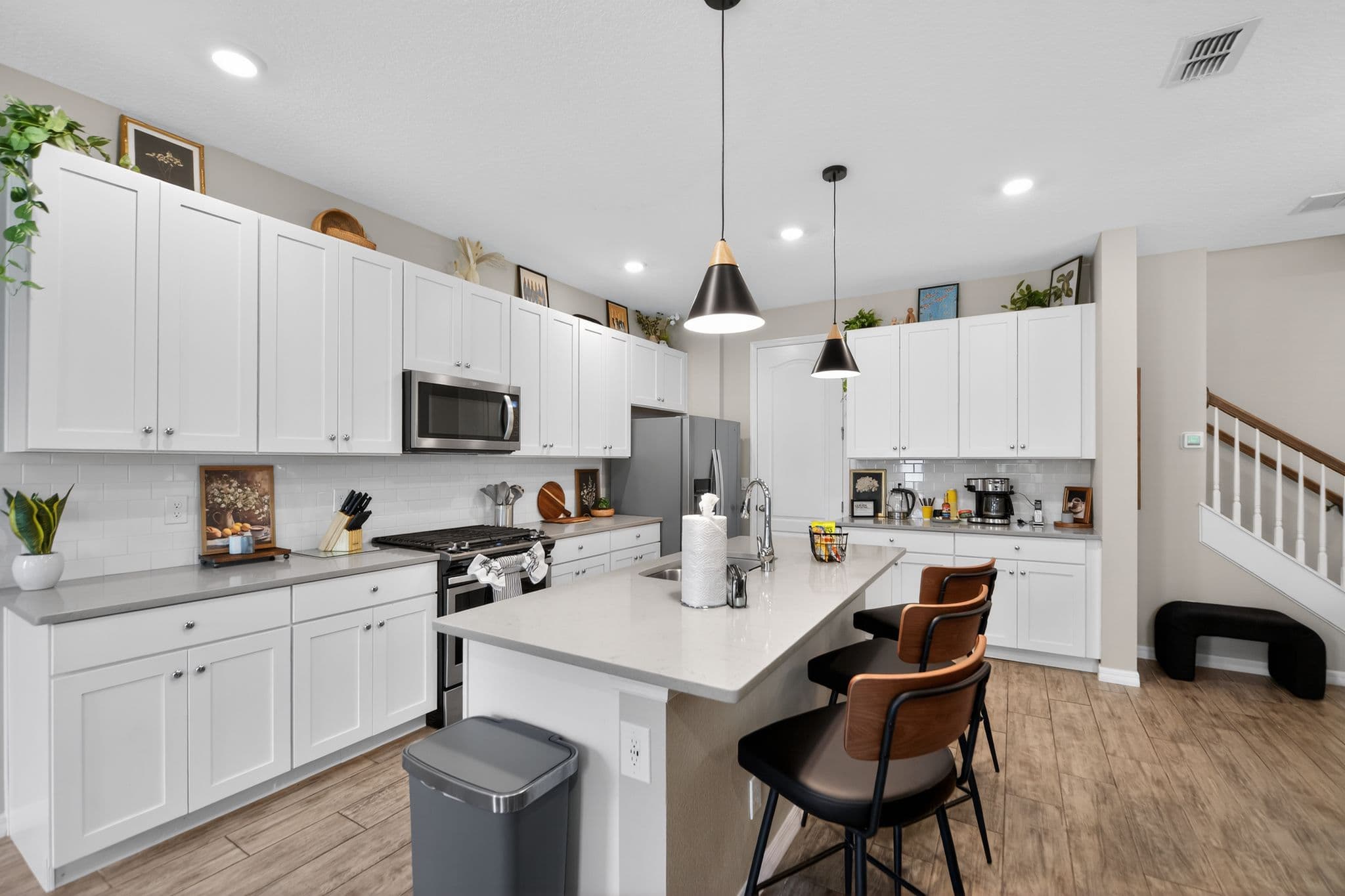 Bright modern kitchen with white cabinets, grey countertops, and an island with three bar stools.