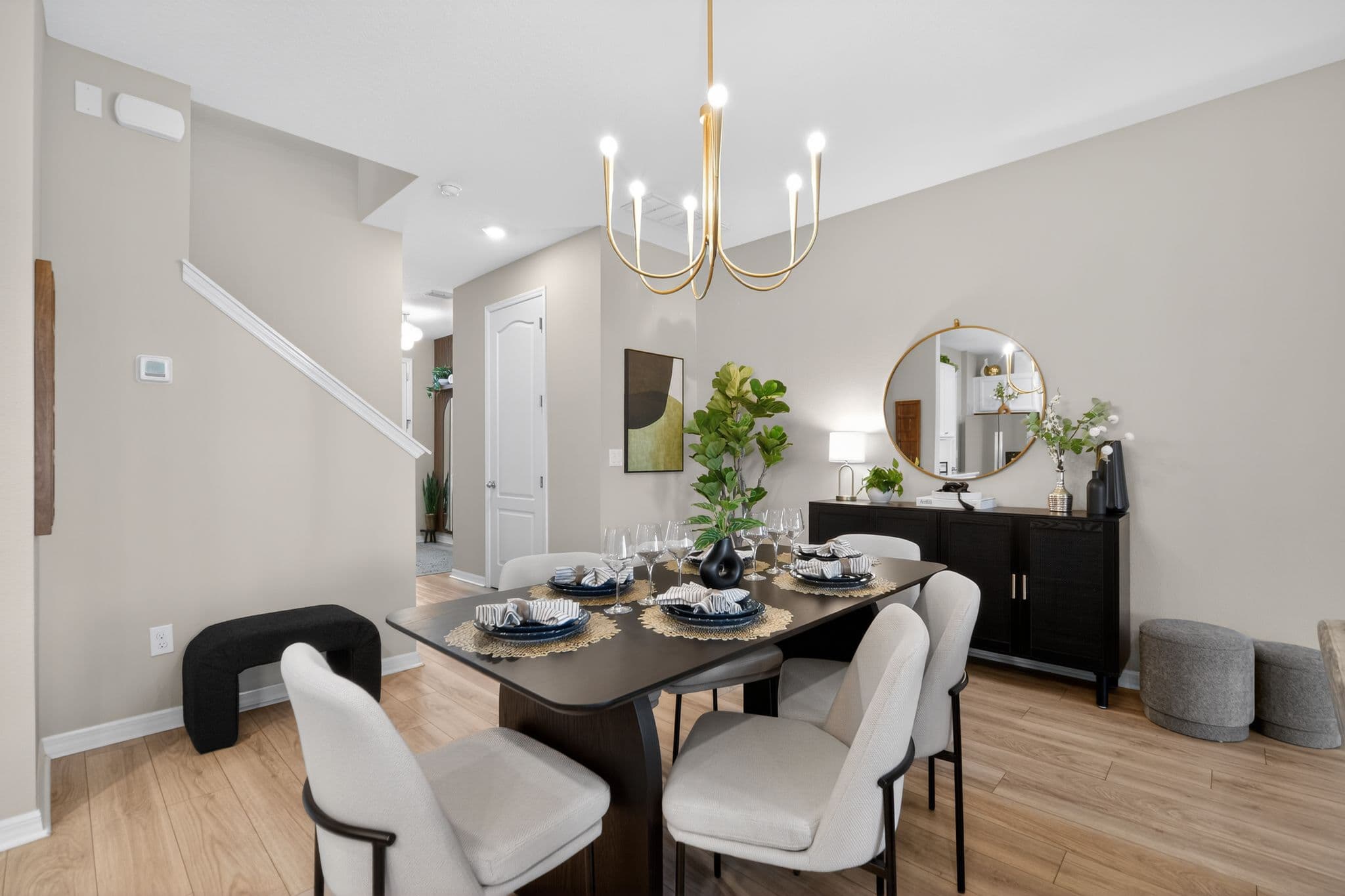 Modern dining room with dark wood table, white chairs, gold chandelier, and a black sideboard.