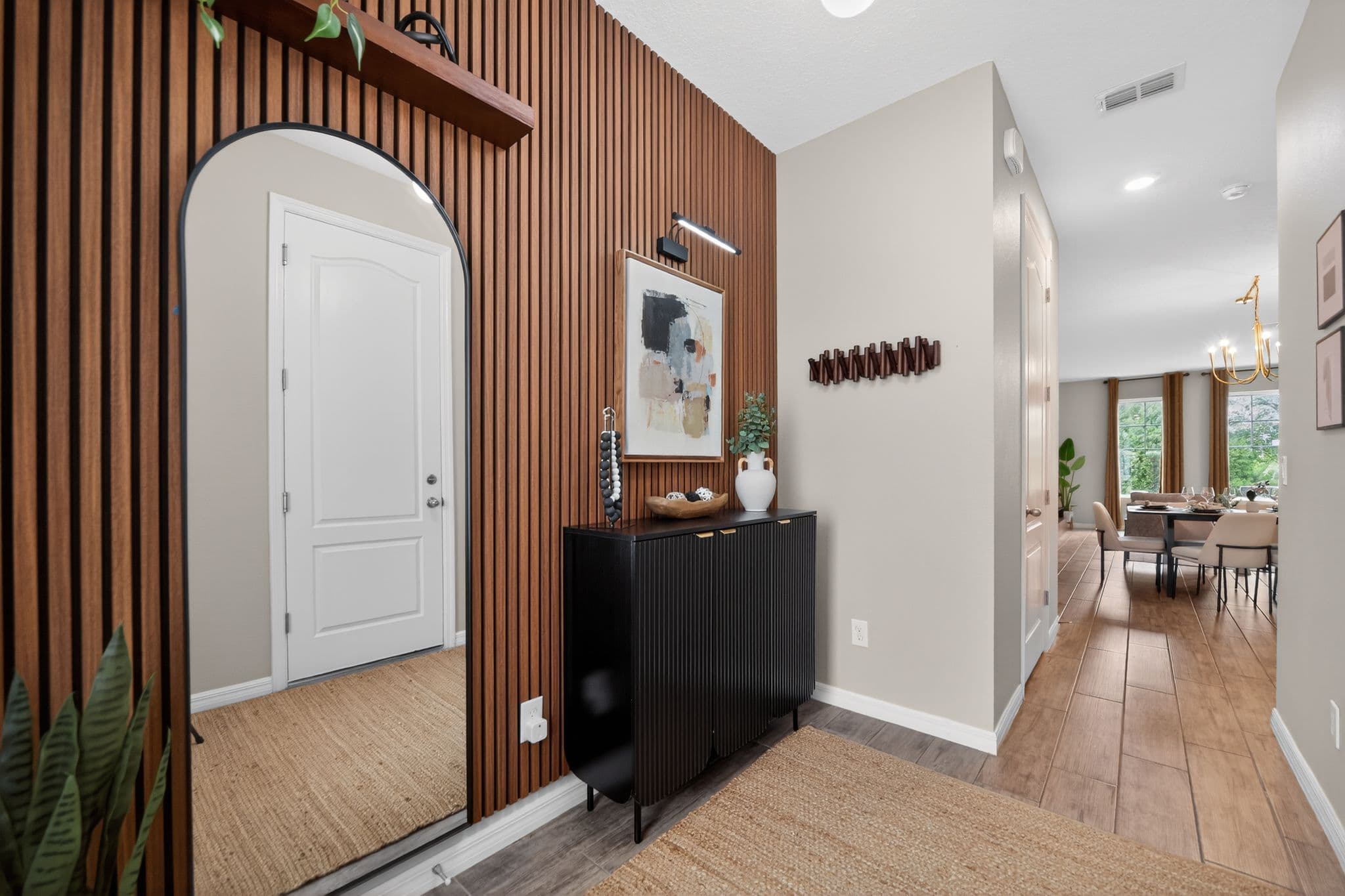 Modern entryway with wood-slat accent wall, arched mirror, black fluted sideboard, and abstract art.