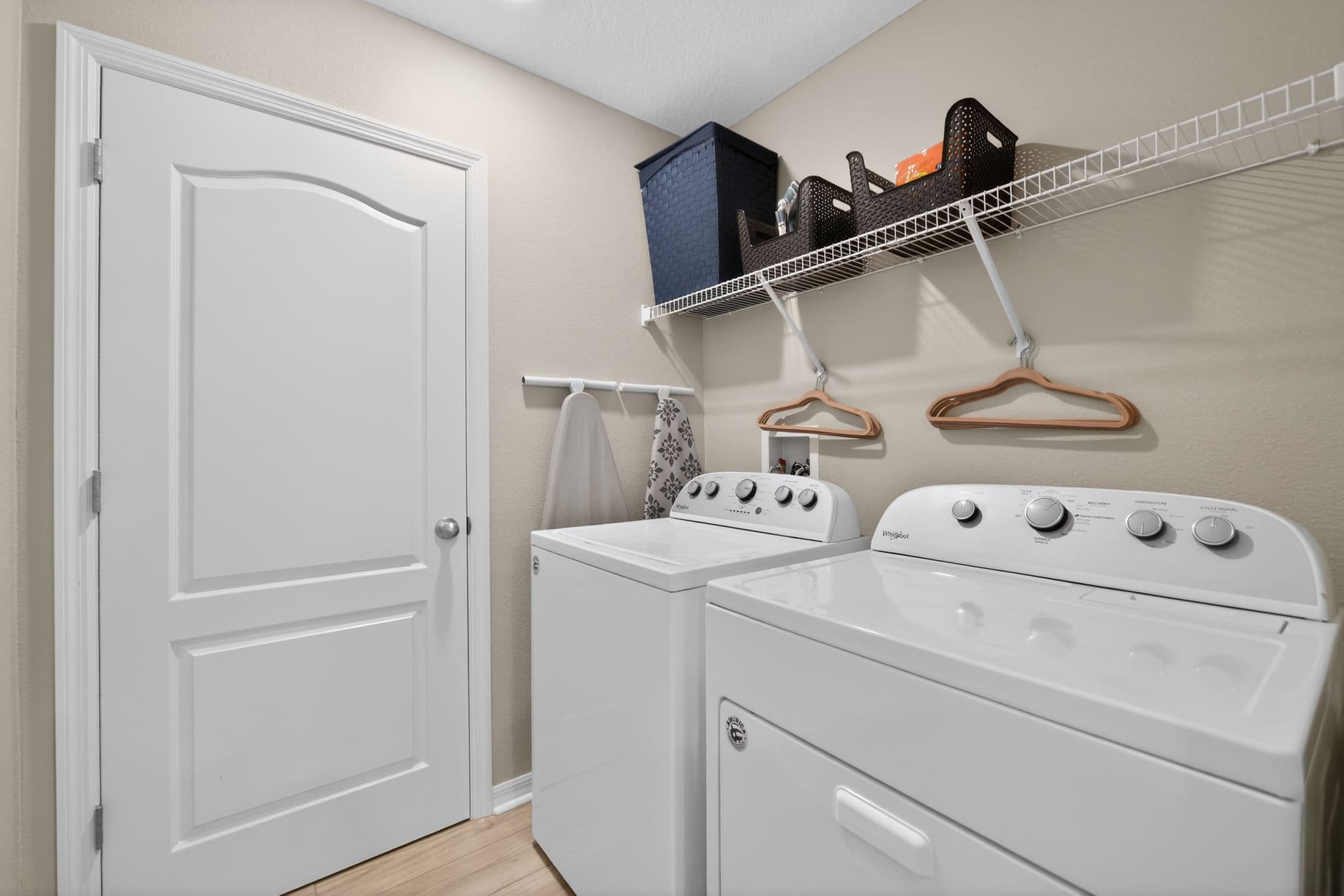 White washer and dryer in a laundry room with overhead wire shelving and storage baskets.